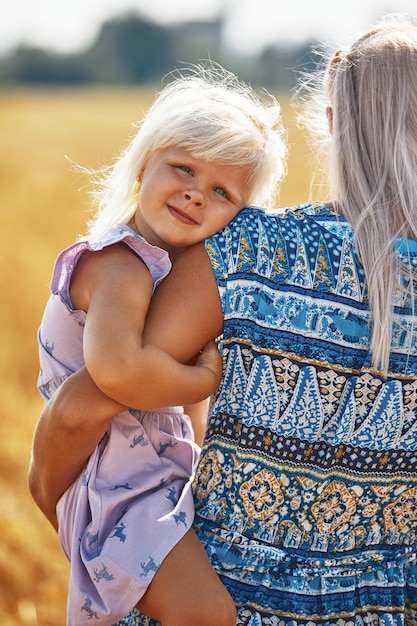 Счастливая мать держит ребенка, улыбаясь на пшеничном поле в солнечном свете