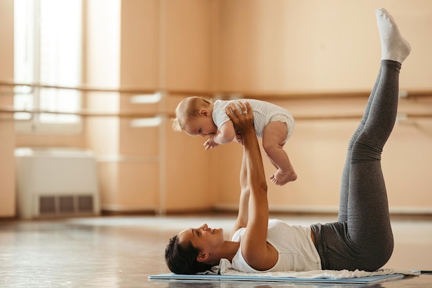 happy mother holding her baby while exercising on the floor in health club