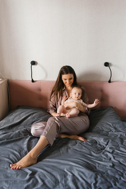 Счастливая мать держит на руках младенца, улыбаясь, сидя на кровати