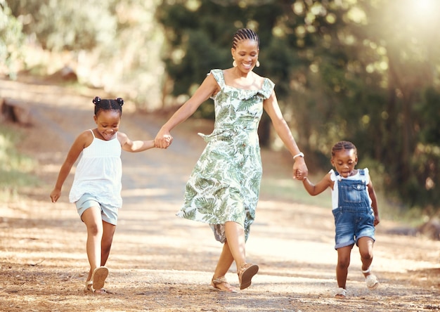 행복한 엄마와 아이들이 즐거운 행복 속에서 자연 속에서 손을 잡고 웃고 있는 숲을 걷고 있는 엄마와 어린 소녀들의 흑인 가족이 자연 야외 환경에서 즐거운 산책을 하고 있습니다
