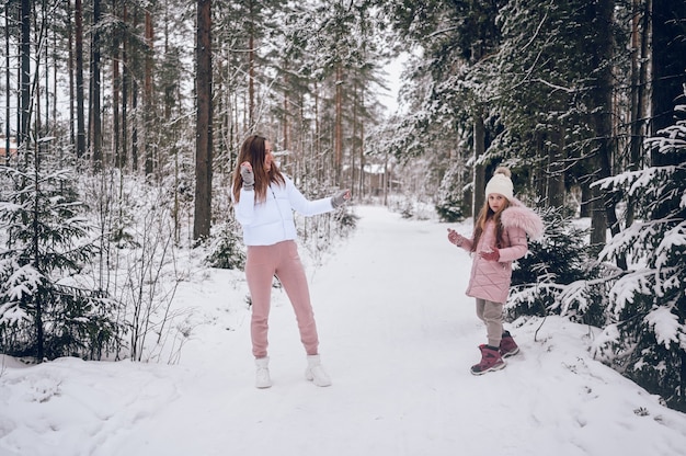 Madre felice e bambina carina in outwear caldo rosa che camminano giocando a palle di neve combattono divertendosi