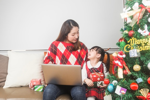 Happy mother and little daughter decorating Christmas tree and gifts at home