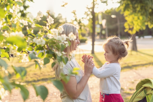 Happy mother and little daughter in the park on a sunny day at sunset Mom and child outdoor Concept of tenderness family single mother flowers smiles hugs mental health harmony holiday