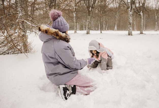 Happy mother and little daughter play snowballs in a snowy\
natural park in a snowfall. great fun moment. spending time\
together on a beautiful cold winter day.