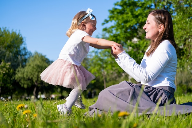 Happy mother and little daughter playing having fun outdoor in park at summer.