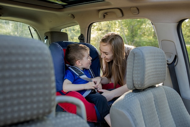 Happy mother looking at her son in a baby seat. Young female preparing kid for a trip. Safety driving concept.