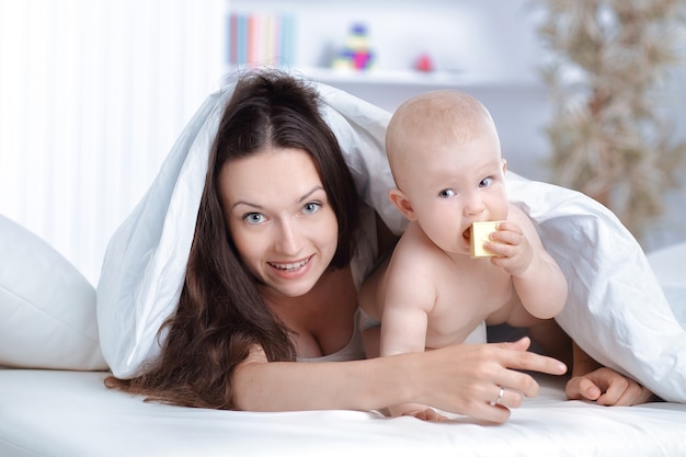幸せな母親は、ベッドに横たわっている赤ちゃんと遊ぶ。教育の概念