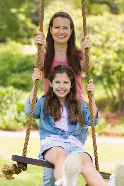 Happy mother pushing daughter on swing