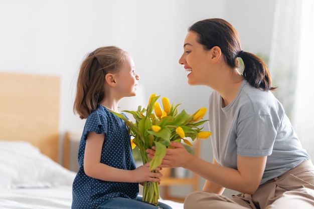 Happy mother's day. Child daughter congratulates mom and gives her flowers. Mum and girl smiling and hugging. Family holiday and togetherness.