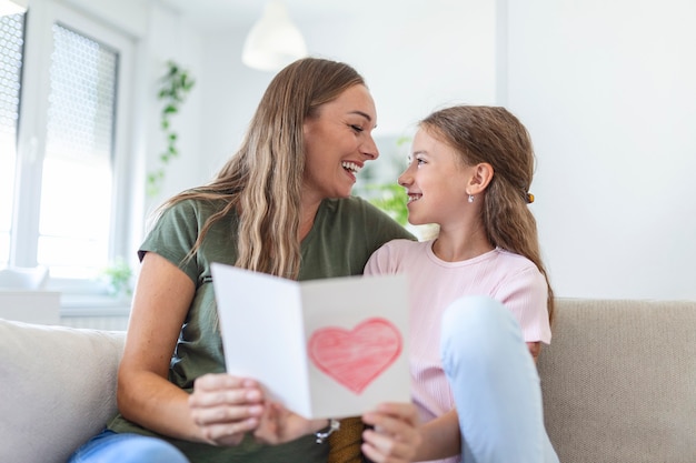 Happy mother's day! Child daughter congratulates mom and gives her postcard. Mum and girl smiling and hugging. Family holiday and togetherness.