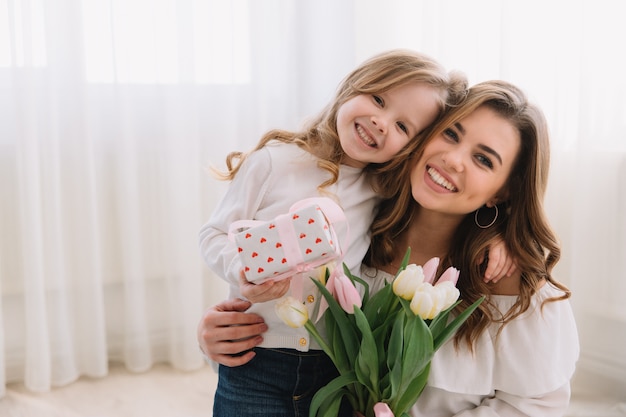 Photo happy mother's day. child daughter congratulates moms and gives her flowers tulips and gift.