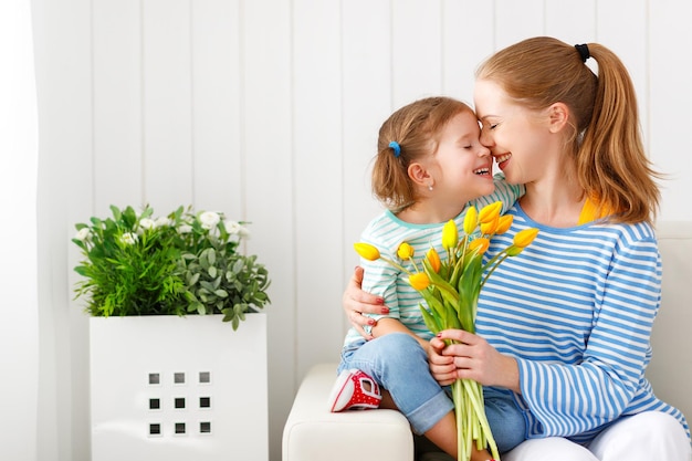 Happy mother\'s day child daughter congratulates moms and gives\
her a postcard and flowers tulips