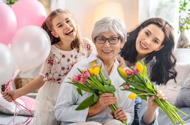 Foto buona festa della mamma la figlia del bambino si congratula con la mamma e la nonna dando loro fiori di tulipani