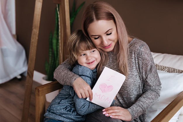 Happy mother's day Child son congratulates mom and gives her postcard Mum and son miling and hugging