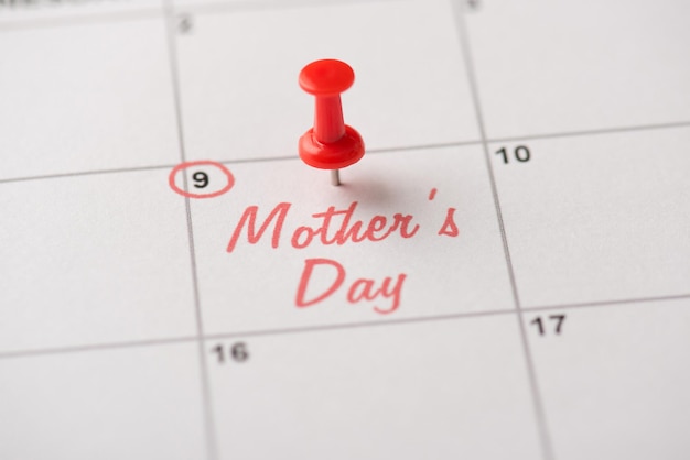 Happy mother's day concept. Cropped close up view photo of red pushpin attached to calendar with inscription mother's day