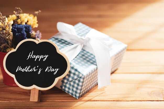 Happy mother's day concept. Gift box with flower, wooden tag on wooden table.