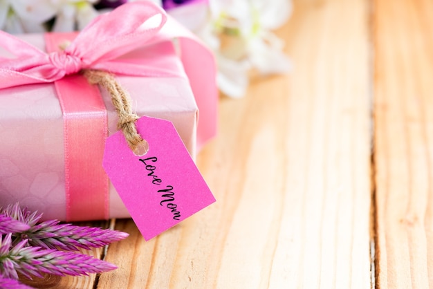 Happy mother's day concept. Gift box with flower, wooden tag on wooden table.