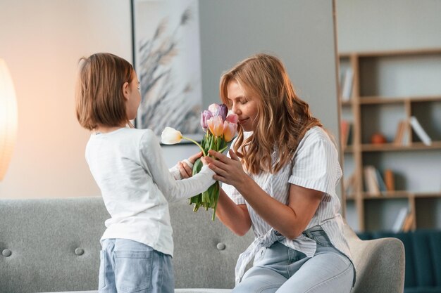 ハッピーマザーズデー 花を贈る 女性と彼女の小さな娘は家庭の部屋で一緒にいます