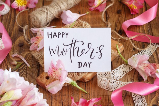 Happy Mother's Day handgeschreven kaart op een houten tafel tussen roze bloemen close-up