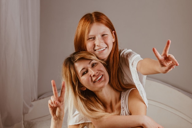 Happy mother's day. Mom and her daughter are playing girl, smiling and hugging in bed. Family holidays and togetherness.