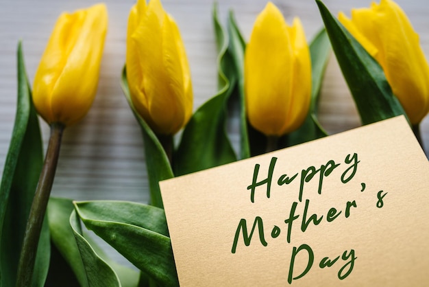 Happy mother\'s day text sign on craft postcard on yellow tulips\
background greeting card concept sensual tender women image holiday\
greeting card for mother\'s day top view flat lay