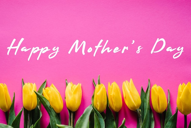 Happy mother\'s day text sign with yellow tulips on pink\
background floral greeting card concept sensual tender women image\
holiday greeting card for mother\'s day top view flat lay