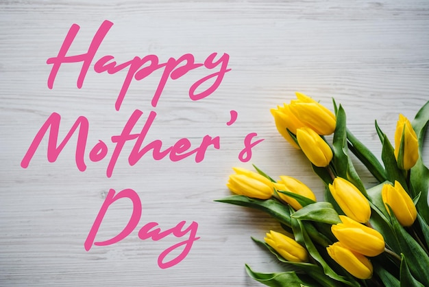 Happy mother\'s day text sign with yellow tulips on white rustic\
wooden background greeting card with flowers concept holiday\
greeting card for mother\'s day top view flat lay