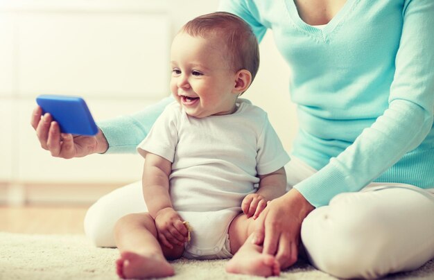 写真 幸せな母親が自宅で赤ちゃんにスマートフォンを見せている