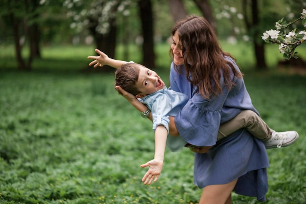 Happy mother and son hug and have fun on a walk in the blossom apple orchard in spring