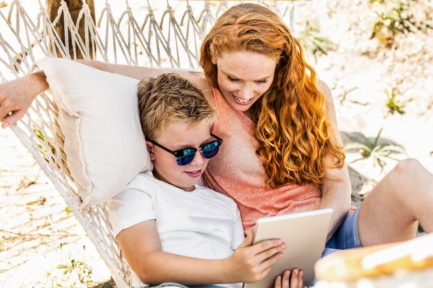 Happy mother and son lying in hammock looking at tablet