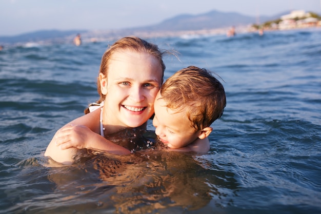 Happy mother teaching her young son to swim