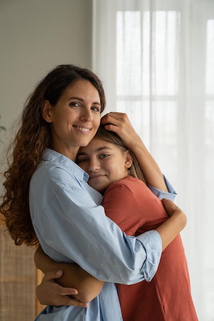 Happy mother and teenage girl daughter cuddling hugging and smiling at camera family bonding