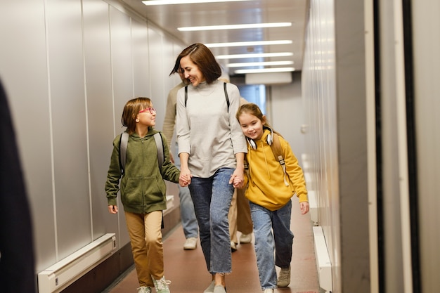 休暇に行く子供たちと一緒に空港ターミナルを歩いている幸せな母親