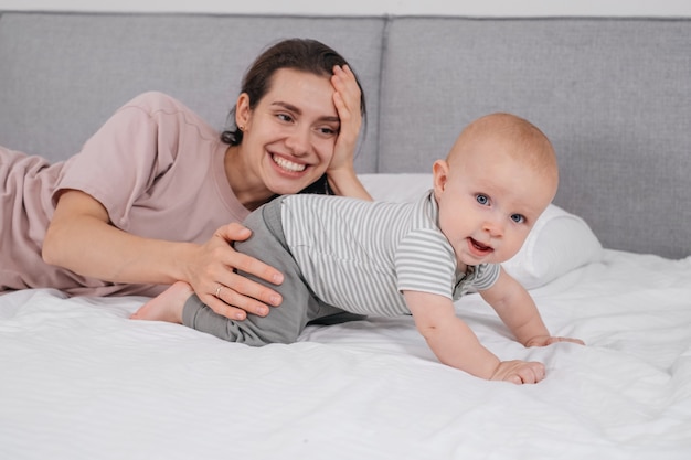 Happy mother with baby boy cuddling in bed playing at home