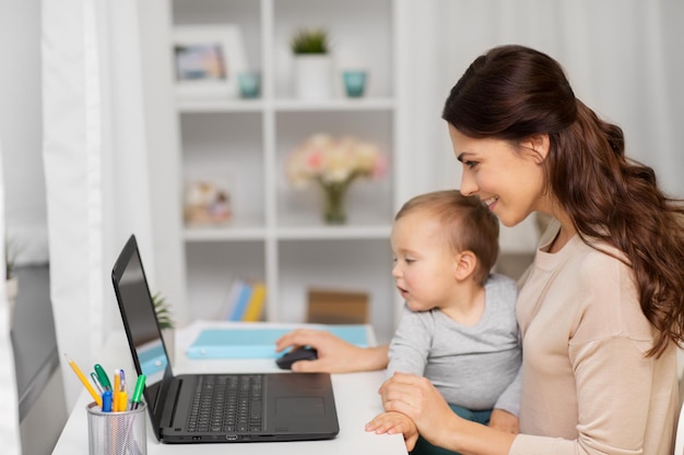 happy mother with baby and laptop working at home
