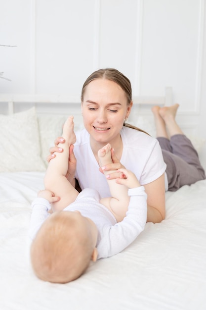 Happy mother with baby playing with his legs on the bed at home