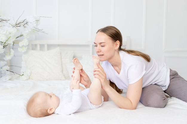 Happy mother with baby playing with his legs on the bed at home