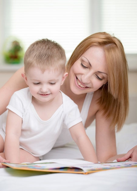 Счастливая мать с книгой чтения младенца дома.