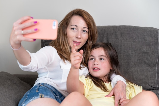 happy mother with her daughter are making a video call to father or relatives in a sofa concept of technology new generation family connection parenthood