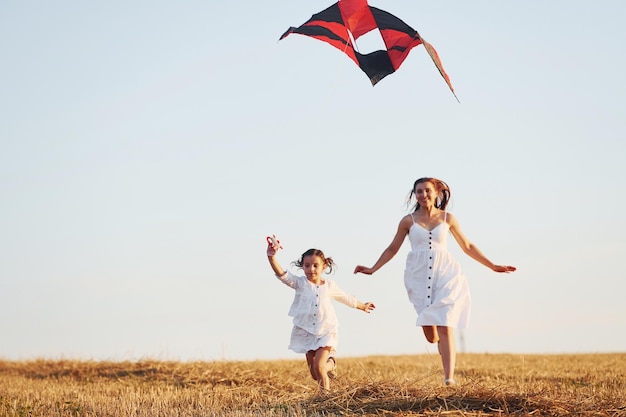 Happy mother with her little daughter have fun by playing with kite outdoors on the field