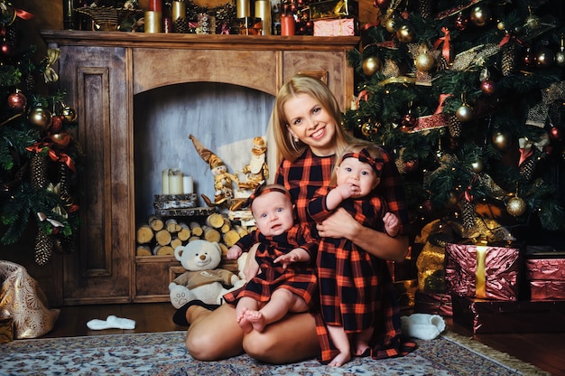 A happy mother with her twin children in the New Year's interior of the house on the background of a Christmas tree.