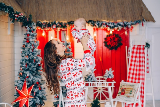 Happy mother with his little daughter in holiday clothing with printed deers and snowflakes in decorated room with a Christmas tree and a wreath