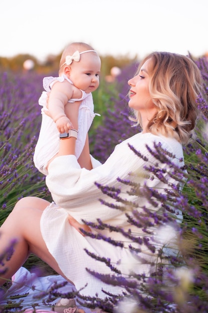 Happy mother with pretty daughter on lavender background. Beautiful woman and cute baby sitting in m