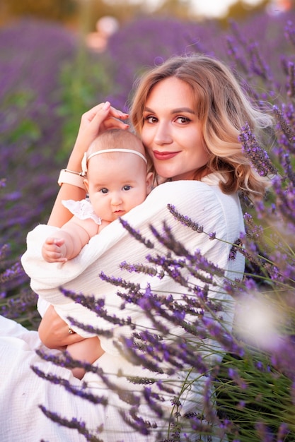 Happy mother with pretty daughter on lavender background. Beautiful woman and cute baby sitting in m