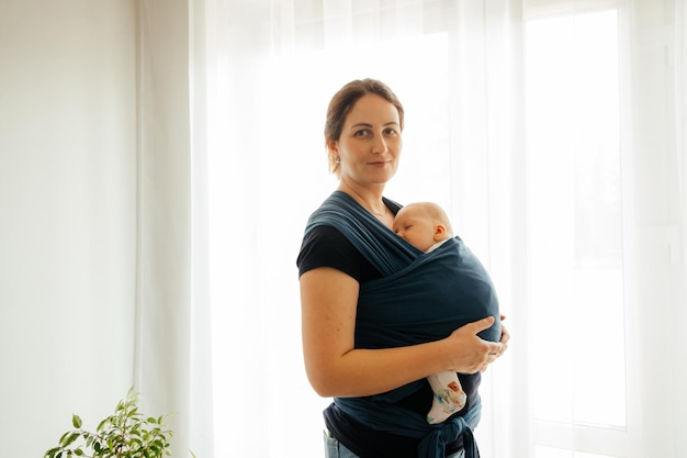 Happy mother with sleeping newborn in baby carrier