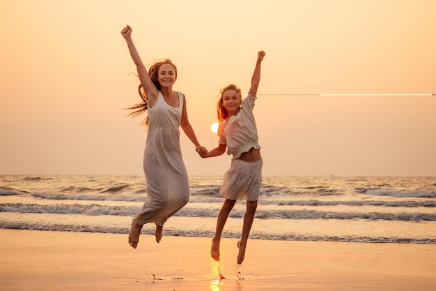 Happy mother and young daughter on the beach at sunset having fun at the seaside playing jumping and rejoicing woman and her child copy space copyspace