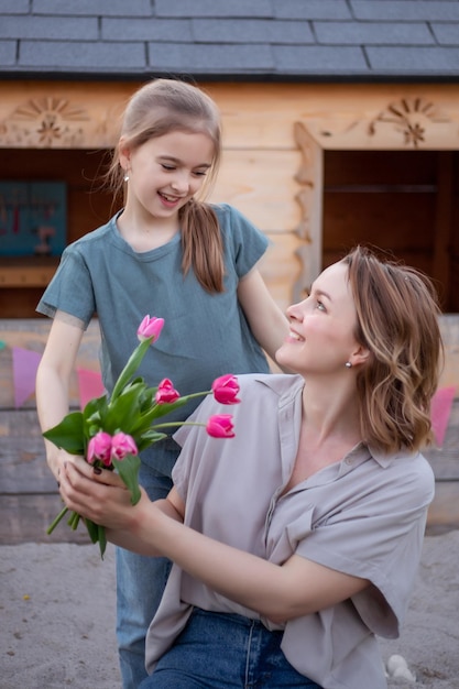 Happy mothers day Child daughter is congratulating mom and giving her flowers tulips Mum and girl smiling and hugging Family holiday and togetherness