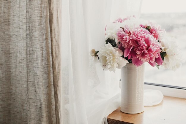 Happy Mothers day Lovely peony bouquet in sunny light on rustic wooden window sill Stylish pink and white peonies in vase on wooden background Copy space Hello spring