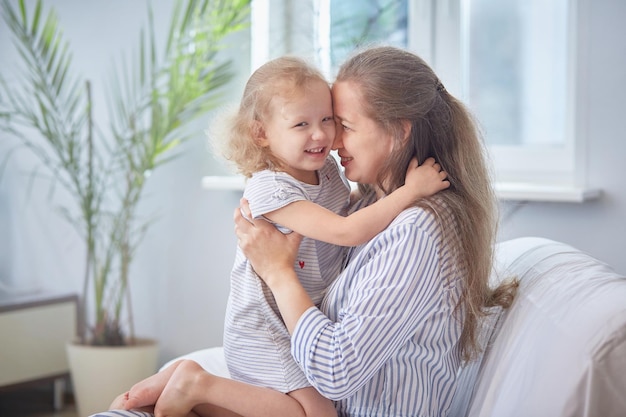 Buona festa della mamma mamma e figlia sorridono e si abbracciano sul divano di casa in una stanza luminosa il concetto di felicità familiare con i bambini vacanze in famiglia e solidarietà