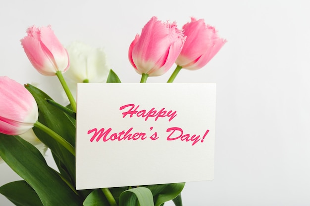 Happy mothers day tekst op cadeaubon in bloemboeket op witte achtergrond. wenskaart voor mama. bloemen bezorgen, gefeliciteerd kaart in bloemen voor vrouwen. wenskaart in roze tulpen.